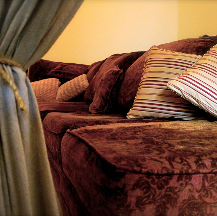 A red couch with pillows on top looms in a close-up shot from our mental health facility. Curtains are coiled together.