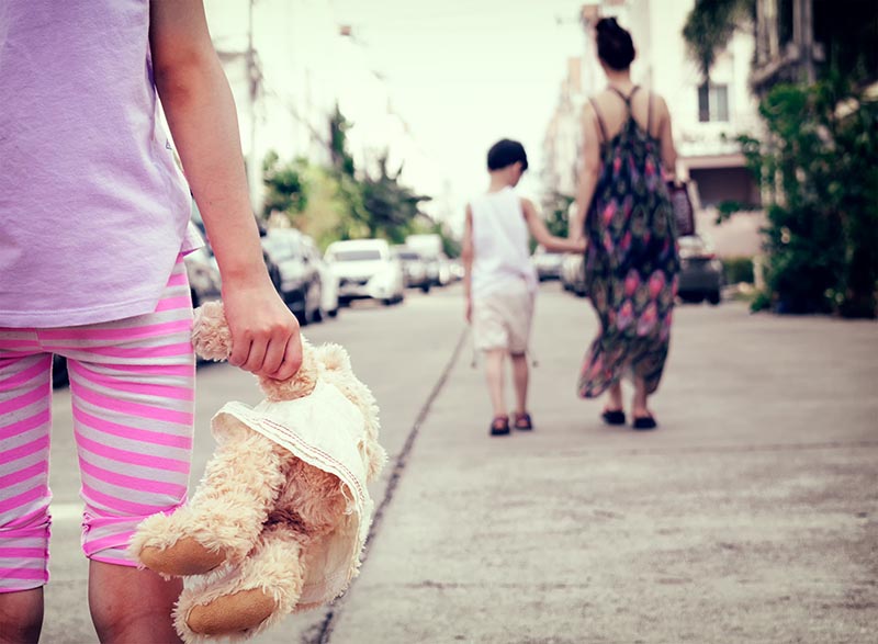 A child holds a teddy bear as their parent walks away, showing the experience of attachment trauma