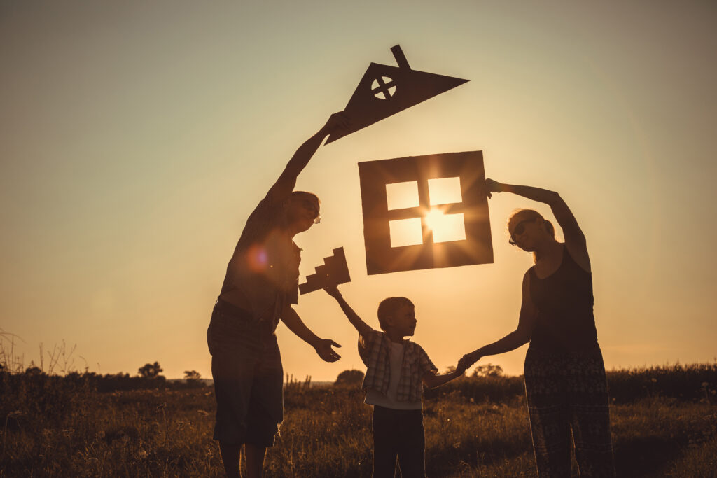  A mother, father, and son stand in a meadow at sunset each holding different pieces of a house etching, representing family dynamics