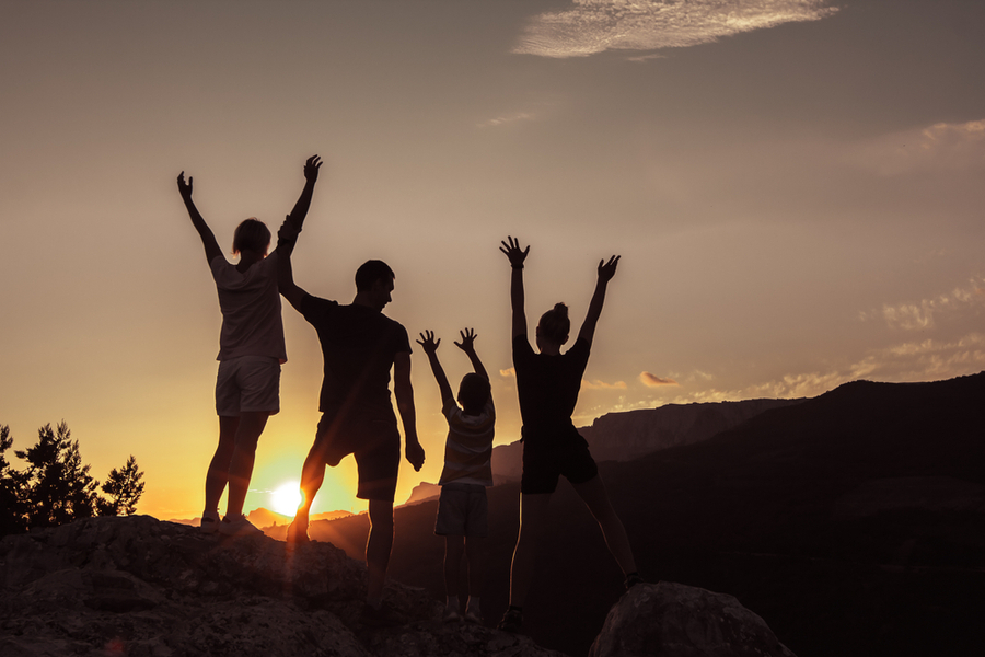 a silhouette of a family who conquered depression standing in front of the sun with arms raised