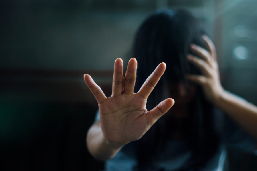 A woman holds one hand to her head and another extended in front of her as she suffers from ptsd