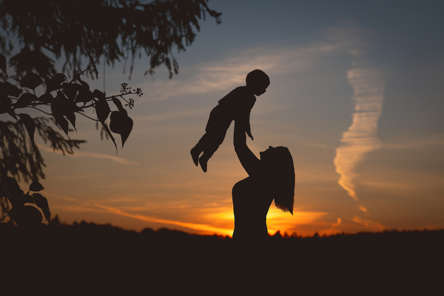 In front of a sunset, a silhouette of a woman lifts a child