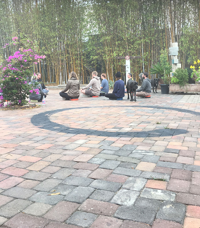 In the distance, nine people sit on our OCD treatment center's cobblestone courtyard in a meditative position.