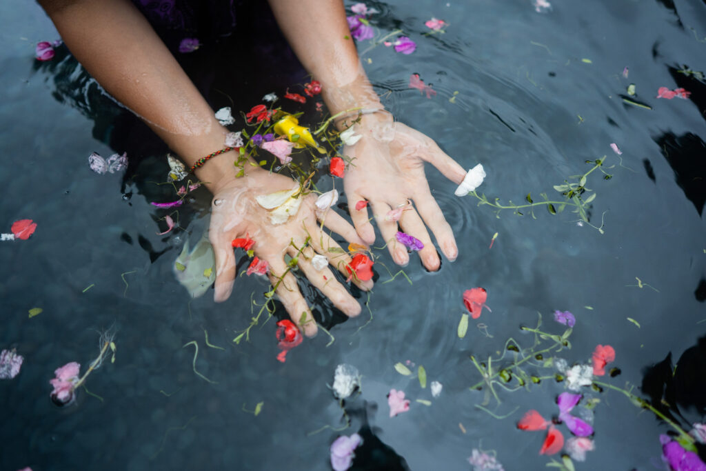 A person palms are face-up in a pool of water as they undergo a spiritual cleanse